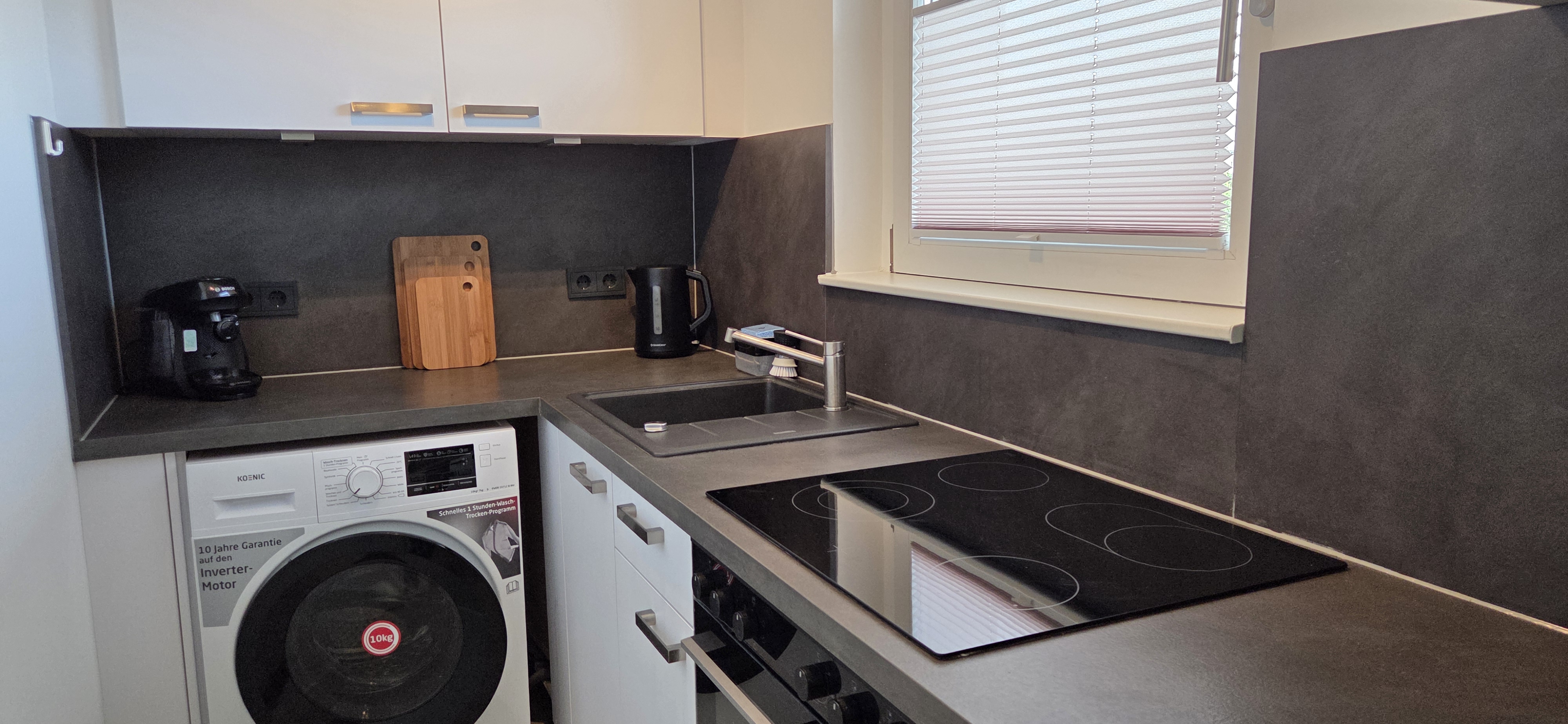 Moderne Einbauküche mit Induktionskochfeld, Backofen und Waschmaschine im Business-Apartment Wedel